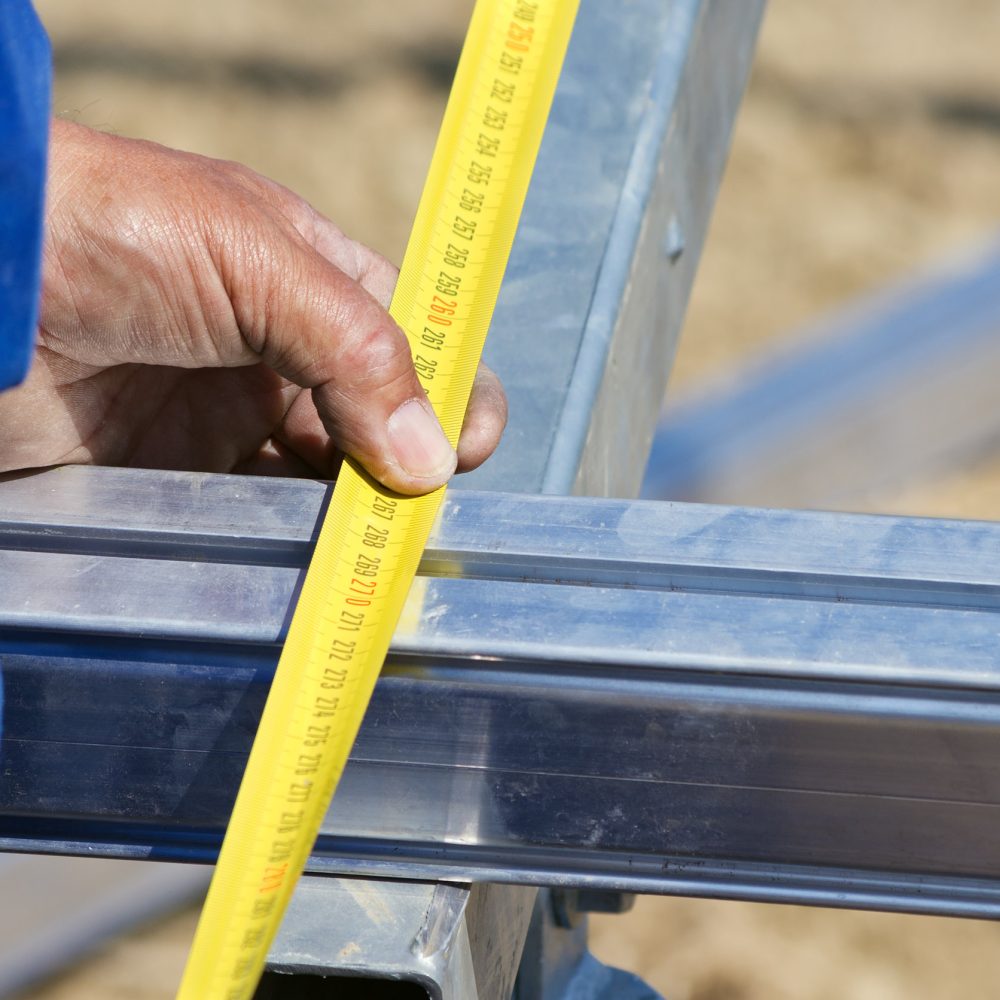 Close up of worker measuring aluminium construction frame with yellow tape